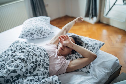 A person wearing a nightshirt and robe sits up in bed, stretching. If you're having trouble getting ...