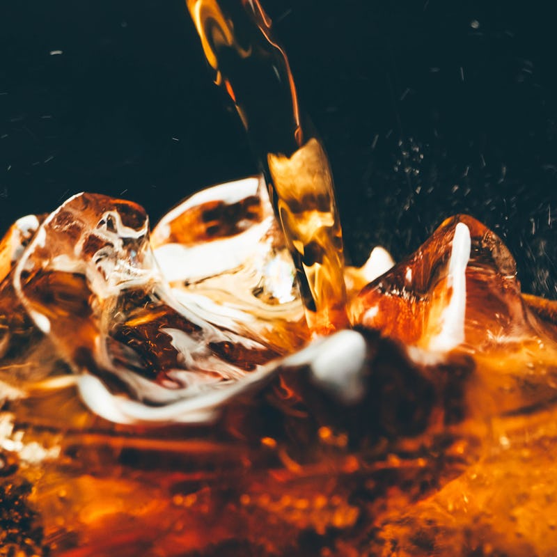 A glass of cold cola with ice cubes. Pouring cola close up.
