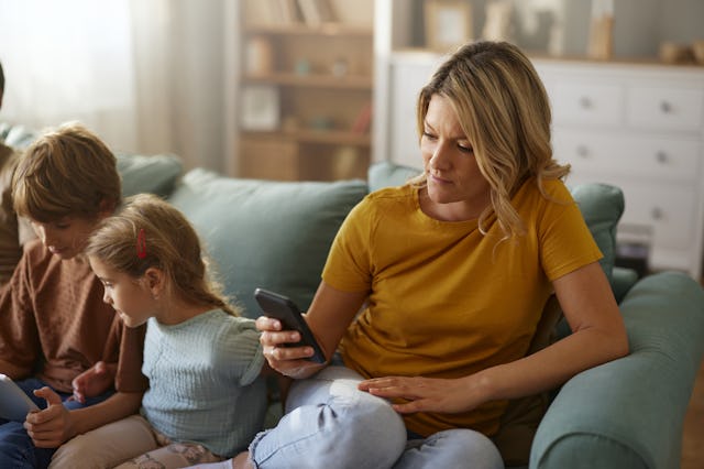 Mother texting next to her kids. "Technoference" occurs when a parent is distracted by their phone, ...