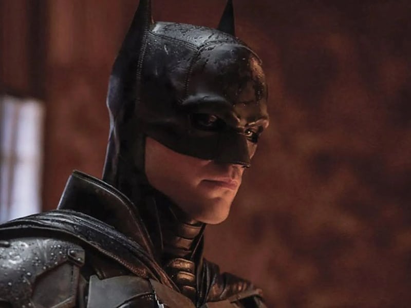 A close-up of Batman in a dark, moody environment, wearing a sleek black suit and mask, with water d...