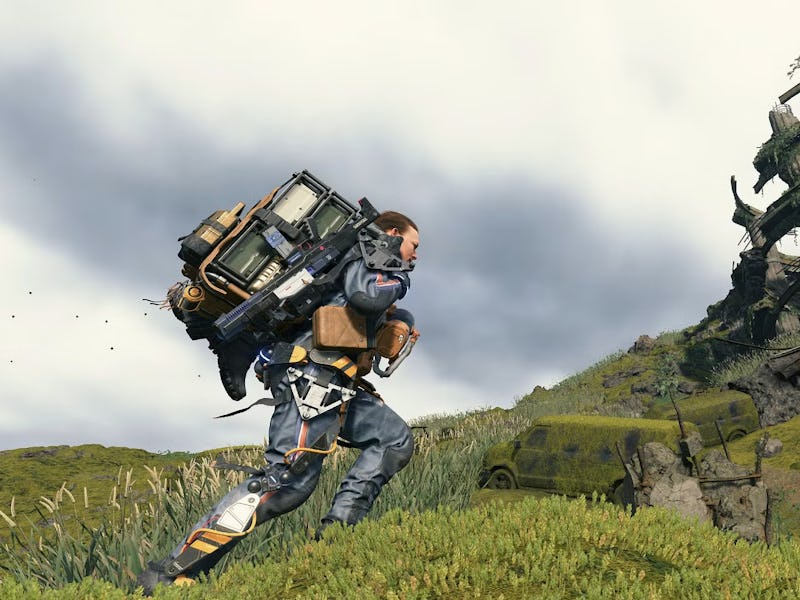 Sam of Death Stranding carrying a large load on his back runs across a grassy landscape, with a futu...